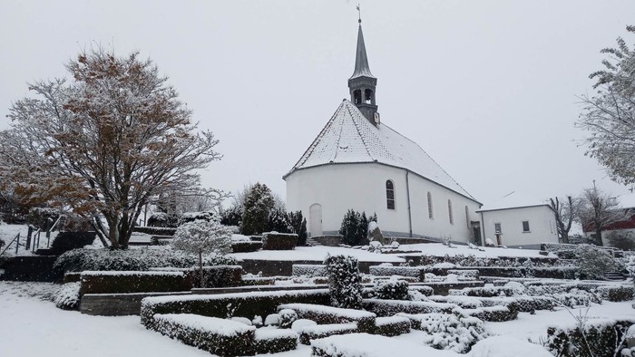 En snede kirke med tårn og omgivelser dækket af sne
