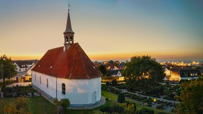 En hvid kirke med rød tag og tårn i en landsby ved sundet