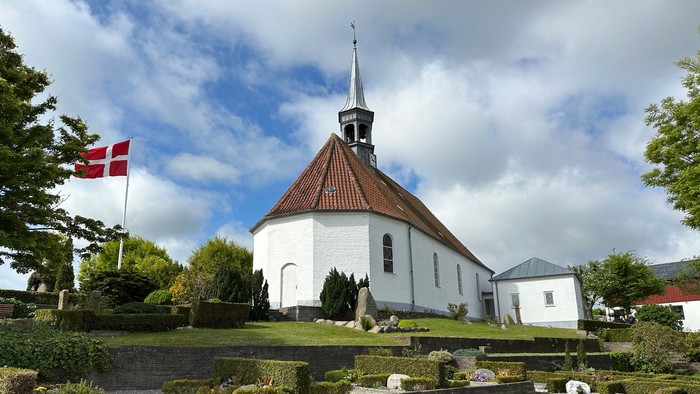 En hvid kirke med spiret og en dansk flag på en grøn plads