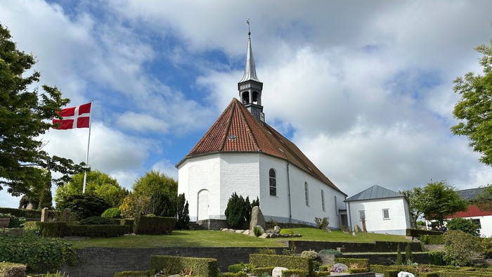 En hvid kirke med spiret og en dansk flag på en grøn plads