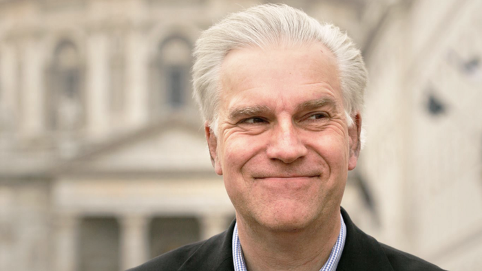 Mand i jakkesæt står foran en kuplet bygning.