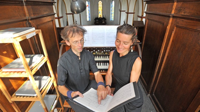 Zwei Personen sitzen in einer Kirche und betrachten ein Buch.