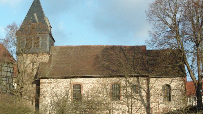 Alte Kirche mit Turm und spitzem Dach, umgeben von Bäumen und Büschen