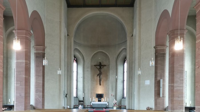 Innenraum einer Kirche mit Holzbanken und Kreuz am Altar