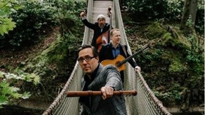 Ein Mann trägt ein Kind auf seinen Schultern, während er über eine Hängebrücke in einem Wald geht.