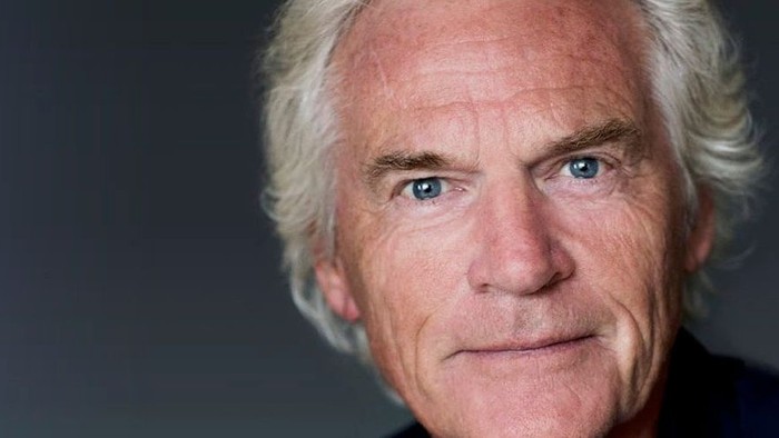 En eldre mand med hvidt hår og blå øjne ser direkte i kameraet.