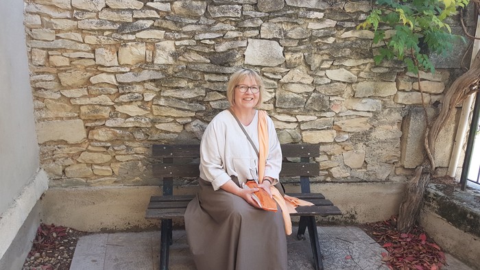 Frau sitzt auf Bank vor Steinmauer