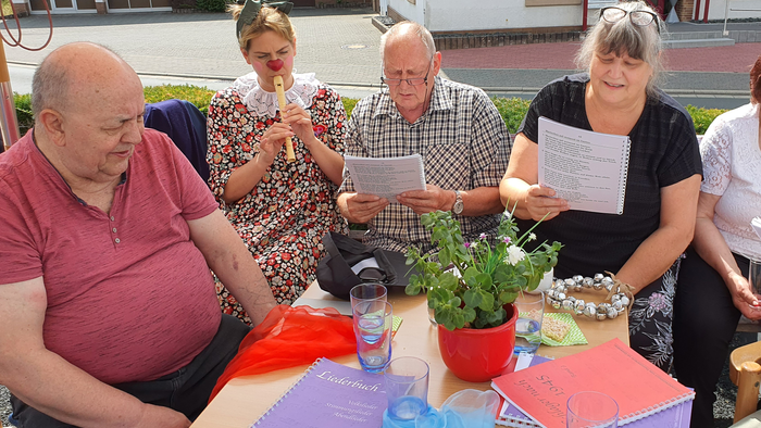 Eine Gruppe älterer Menschen sitzt an einem Tisch und hält Blätter in den Händen.