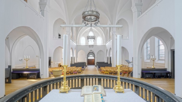 Indre del af en stor, lys kirke med høje buegange og centralt belysning.