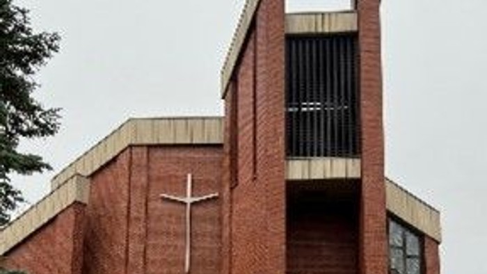 Das Bild zeigt eine moderne Ziegelkirche mit Kreuz und hohem Turm.