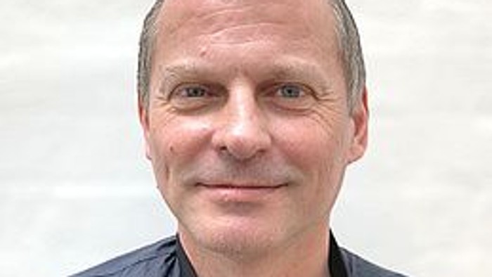 En middlealder mand med kort hår og blå jacke.