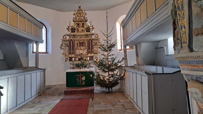 In der Kirche steht ein geschmückter Weihnachtsbaum vor einem Altar.