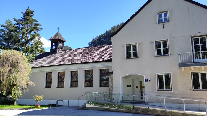 Ein großes, weißes Gebäude mit einem Uhrturm und einem Balkon, umgeben von Bäumen und Gras.