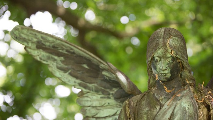 Die Bronzestatue eines Engels mit grünem Patina steht vor Bäumen