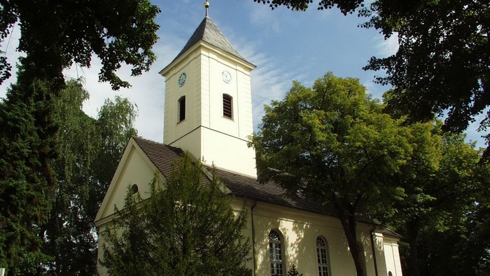 Kleine weiße Kirche mit Uhrturm zwischen Bäumen