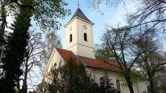 Weiße Kirche mit Uhrturm und rotem Dach zwischen Bäumen