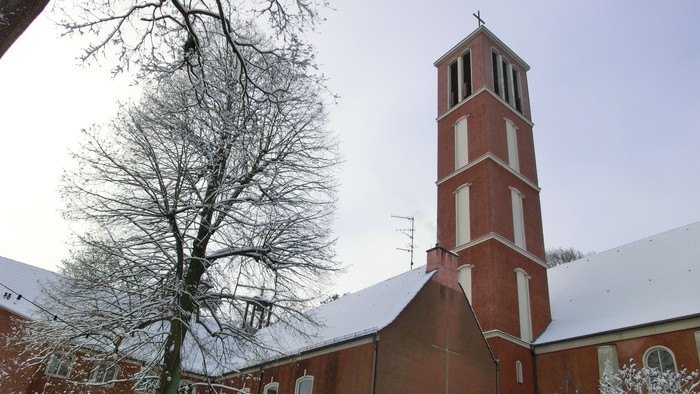 Weiß überzogene Kirche mit hohem Turm und kahlen Baum davor