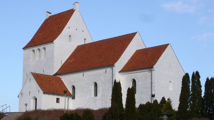 Hvid kirke med røde tagtegn og træer foran