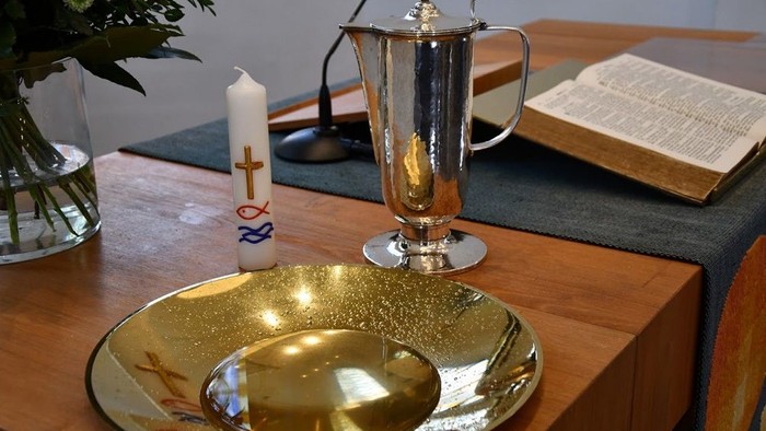 Auf dem Tisch stehen ein silberner Kelch, eine goldene Schale und eine Kerze vor einem Buch