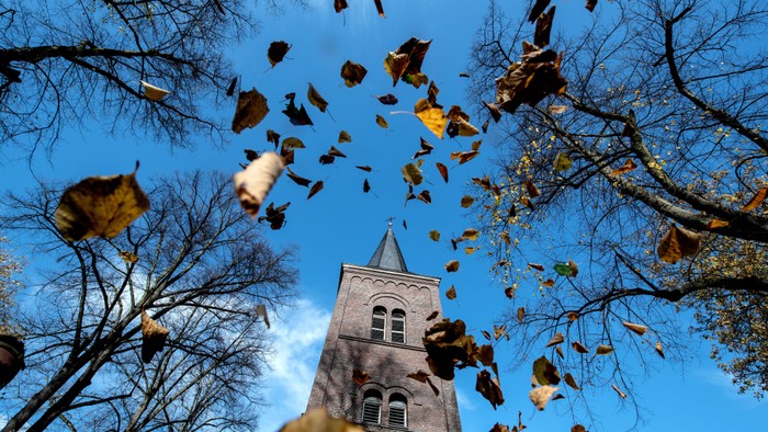 Herbstblätter fallen vor einem Kirchturm vom klaren blauen Himmel