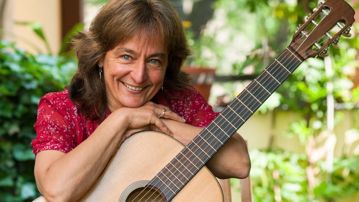 Eine Frau sitzt mit einer Gitarre im Freien.