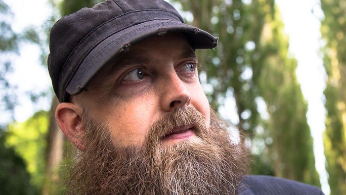 Mand med skæg og hat, der kigger op.