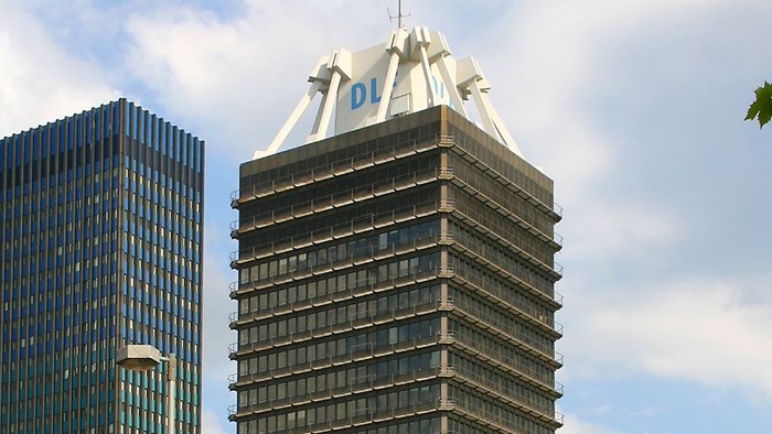 Zwei hohe Gebäude mit "01" und "Kolin" Beschriftung, Bäume, Himmel