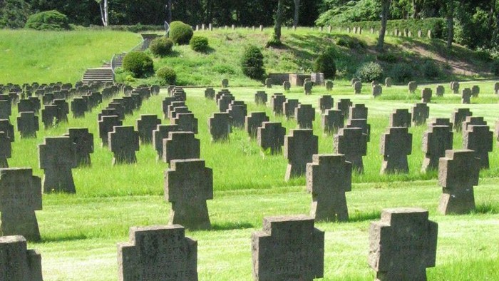 Ein Friedhof mit vielen Grabsteinen auf einem grasbewachsenen Hügel.