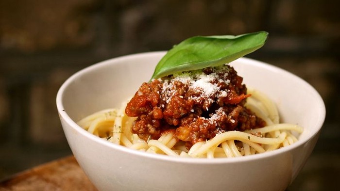 En bolle med spaghetti i tomatsoace, garnished med frisk basilika og parmesan.