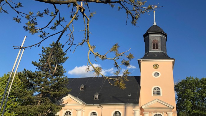 Kirche mit hohem Turm und Uhr, umgeben von Bäumen unter blauem Himmel
