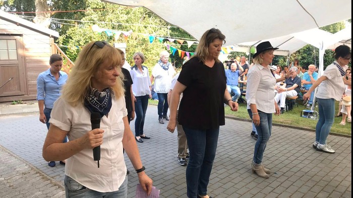 Eine Gruppe von Menschen tanzt unter einem Zelt auf einem Kopfsteinpflasterplatz.