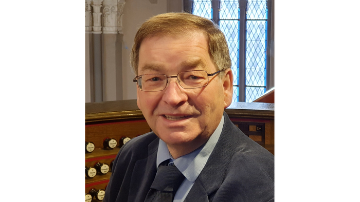 Man in suit and glasses standing in front of organ pipes.