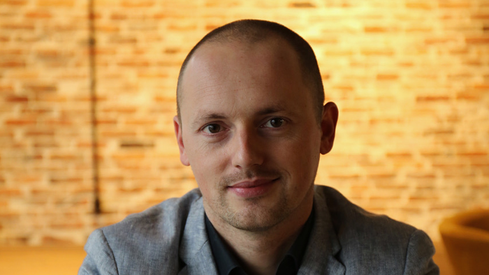 A man with a shaved head wearing a gray suit jacket.
