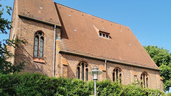 Alte Kirche mit rotem Dach und hohem Turm, umgeben von Grün.
