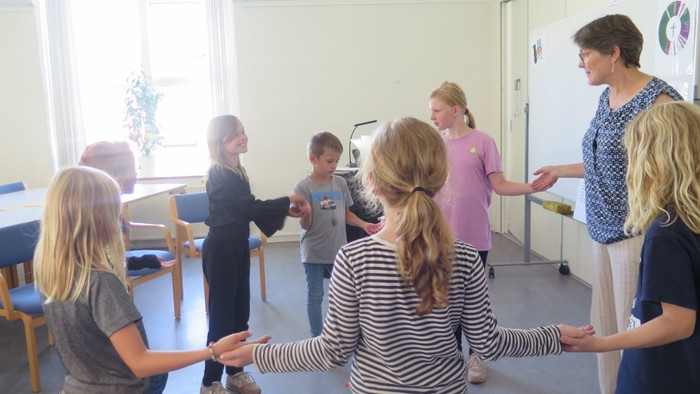 En gruppe af voksne og børn står i en hal og holder hånd i en kreds.