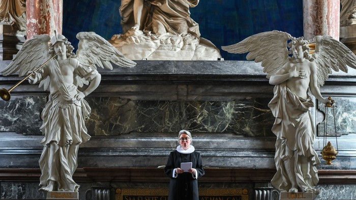 En præst står i en prægtig kirke med store skulpturer og billeder af engle.