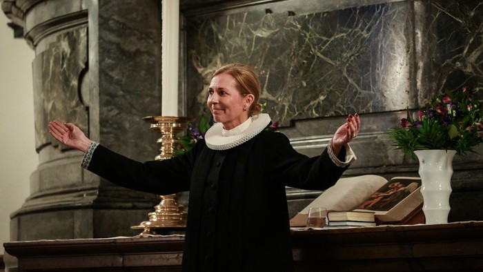 Kvinde i mørkt kapel i kirke med udbrede arme.