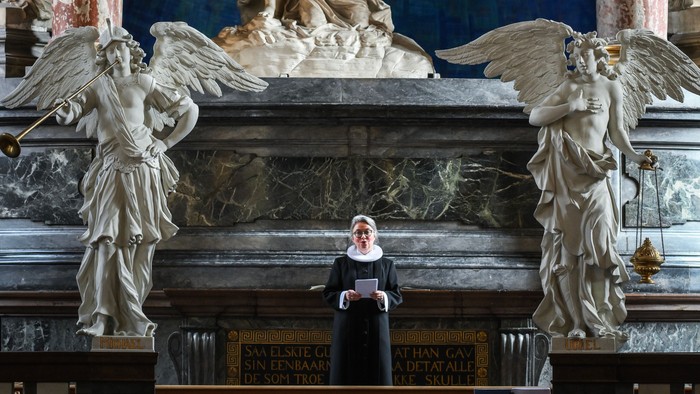 En præst står i en prægtig kirke med store skulpturer og malerier.