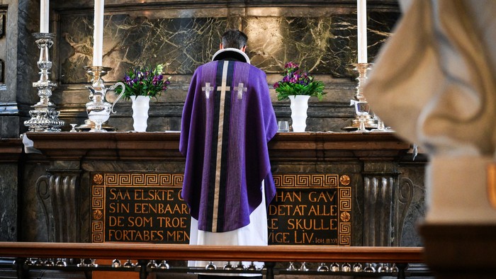 Et religiøst alter med en lilla kåbe, stearinlys og latinsk tekst.