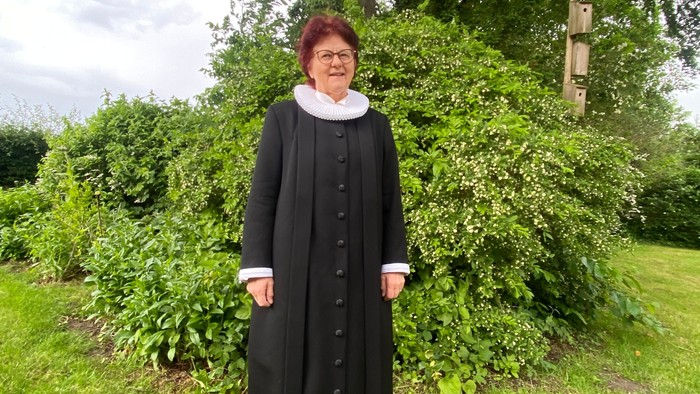 En kvinde i svart nonneklæde står i en have.