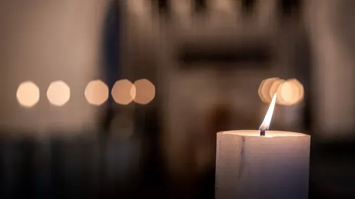 En lysende stearinlys i forgrunden, omgivet af udeblænde lys.