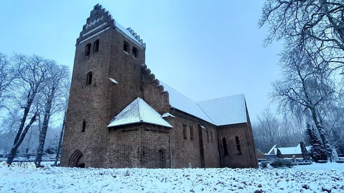 Historisk murstenskirke dækket af sne med en flagstang, der viser et flag om vinteren.