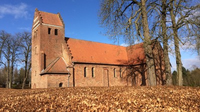 En gammel kirke med røde teglsten og tårn, omgivet af løvfald og træer