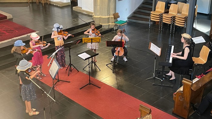 Eine Gruppe von Musikern spielt in einem Kirchenraum verschiedene Streichinstrumente.