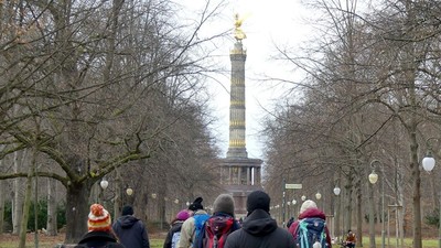 Ein Gruppe von Menschen geht in einem Park auf eine Säule zu
