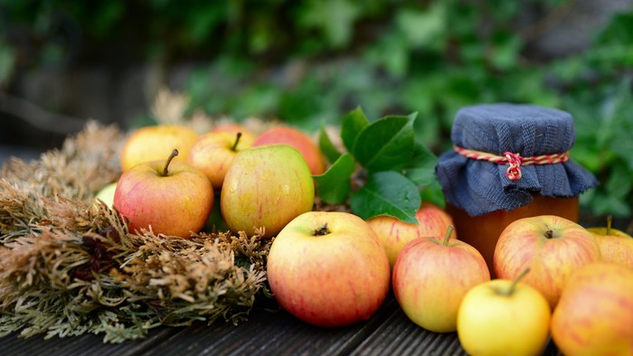 Ein Haufen Äpfel und ein Glas Konfitüre auf einem Holztisch im Freien