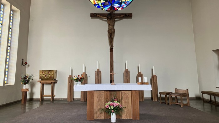 Die Kirche mit einem großen buntem Rundfenster und einem Kruzifix davor