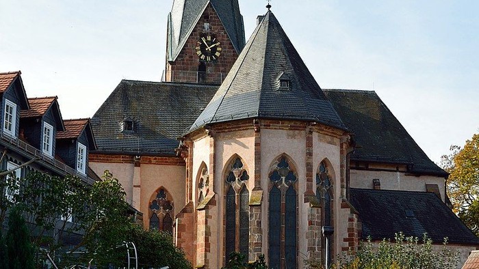 Kirche mit hohem Turmspitz und Uhrturm, umgeben von Bäumen und Gebäuden.
