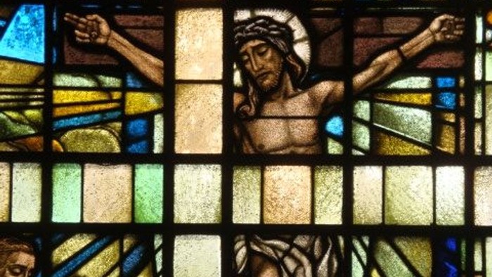Das Glasfenster zeigt Jesus am Kreuz mit zwei Gestalten darunter