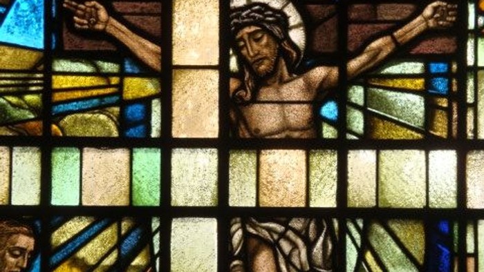 Das Glasfenster zeigt Jesus am Kreuz mit zwei Gestalten darunter